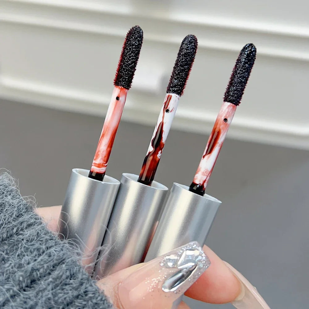 Close-up of three XMSJ Waterproof Peel-Off Lip Tint applicators in matte silver tubes with deep red tint, held in hand with nail art BeTrendy